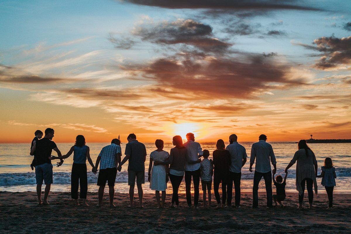 A diverse group of people holding hands together at sunrise